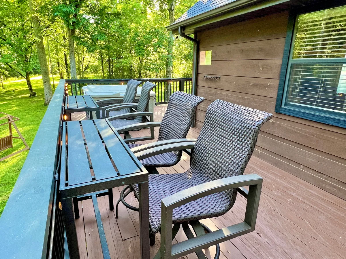 A sun-dappled deck with comfortable seating, a bubbling hot tub, and a wooden railing overlooking treetops. This space blends comfort with the surrounding natural landscape, inviting guests to soak or lounge while immersed in the outdoors.