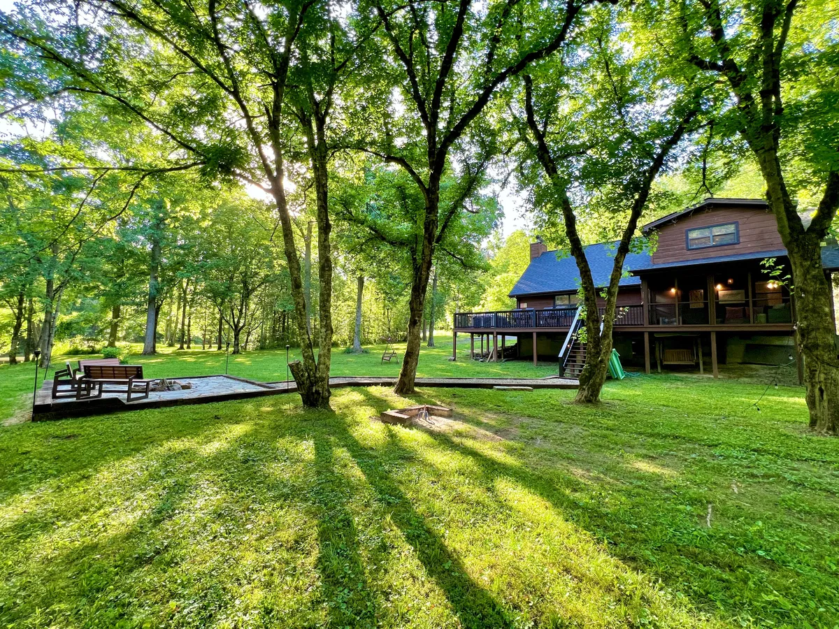 An inviting backyard space with a view of the house, surrounded by trees, a patio area, and a cozy fire pit. The setup hints at evening gatherings, barbecues, or quiet moments under the open sky.