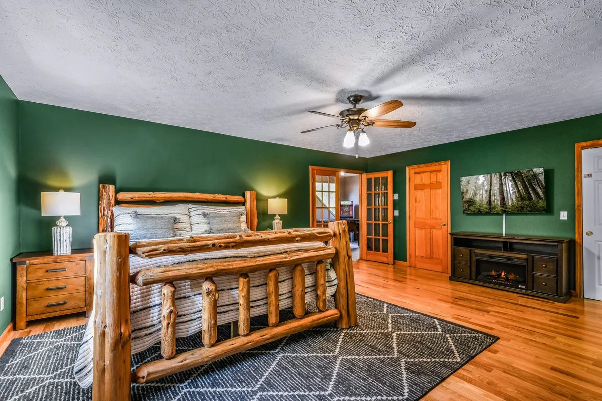 This image features a rustic log bed with nightstands and lamps flanking either side, and a fireplace providing a cozy focal point. The room exudes mountain cabin charm and comfort, ideal for relaxation after a day of adventure.