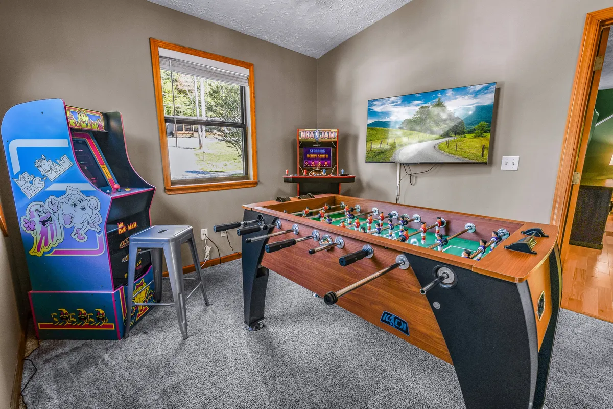 This image captures a vibrant game loft setup featuring a foosball table, a classic arcade game machine, and a television. The overall ambiance is fun and relaxed, perfectly suited for group activities and friendly competition.