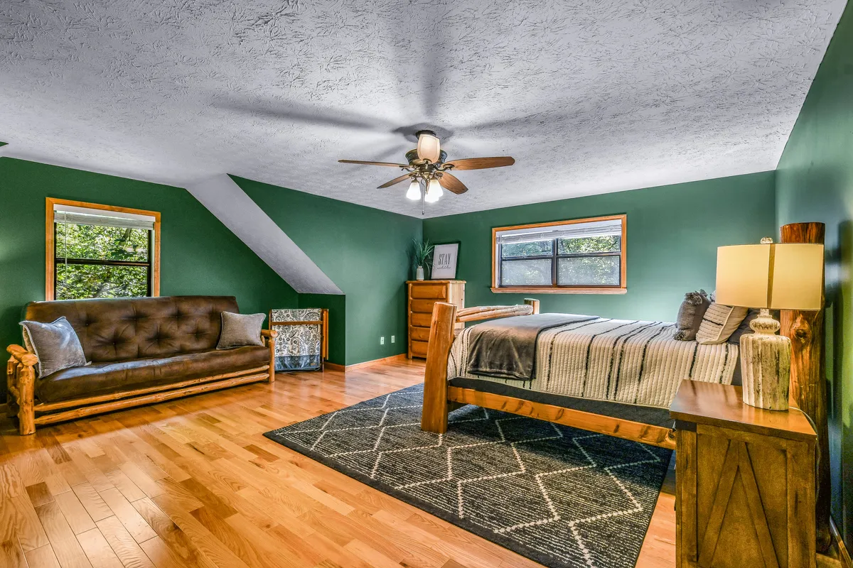 A welcoming bedroom with a wooden bed, plush sofa, nightstand, rug, and large windows letting in natural light. The room feels spacious and inviting, perfect for restful sleep or quiet moments.