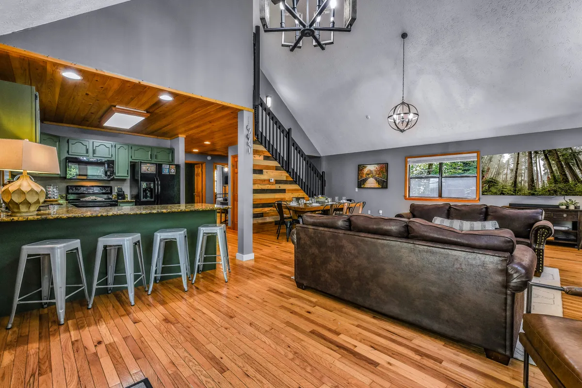 A warm, inviting interior with a kitchen island and bar stools, a farmhouse dining table, comfortable leather couches, and a staircase leading to an upper level. The scene balances spaces for cooking, dining, and relaxing, emphasizing opportunities for socializing and shared experiences.