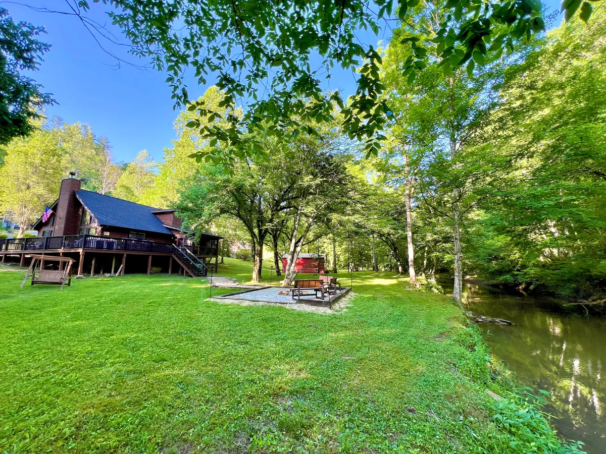 This view captures the house with the nearby creek and a picnic area set beneath the trees. The landscape invites exploration and moments of quiet, with opportunities for picnics, light play, and easy access to nature trails or the creek itself. The setting is peaceful and ideal for families—including four-legged members—seeking outdoor enjoyment.